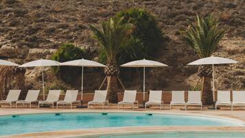 Zona de piscina con sillones de descanso y sombrillas, rodeada por un paisaje montañoso.