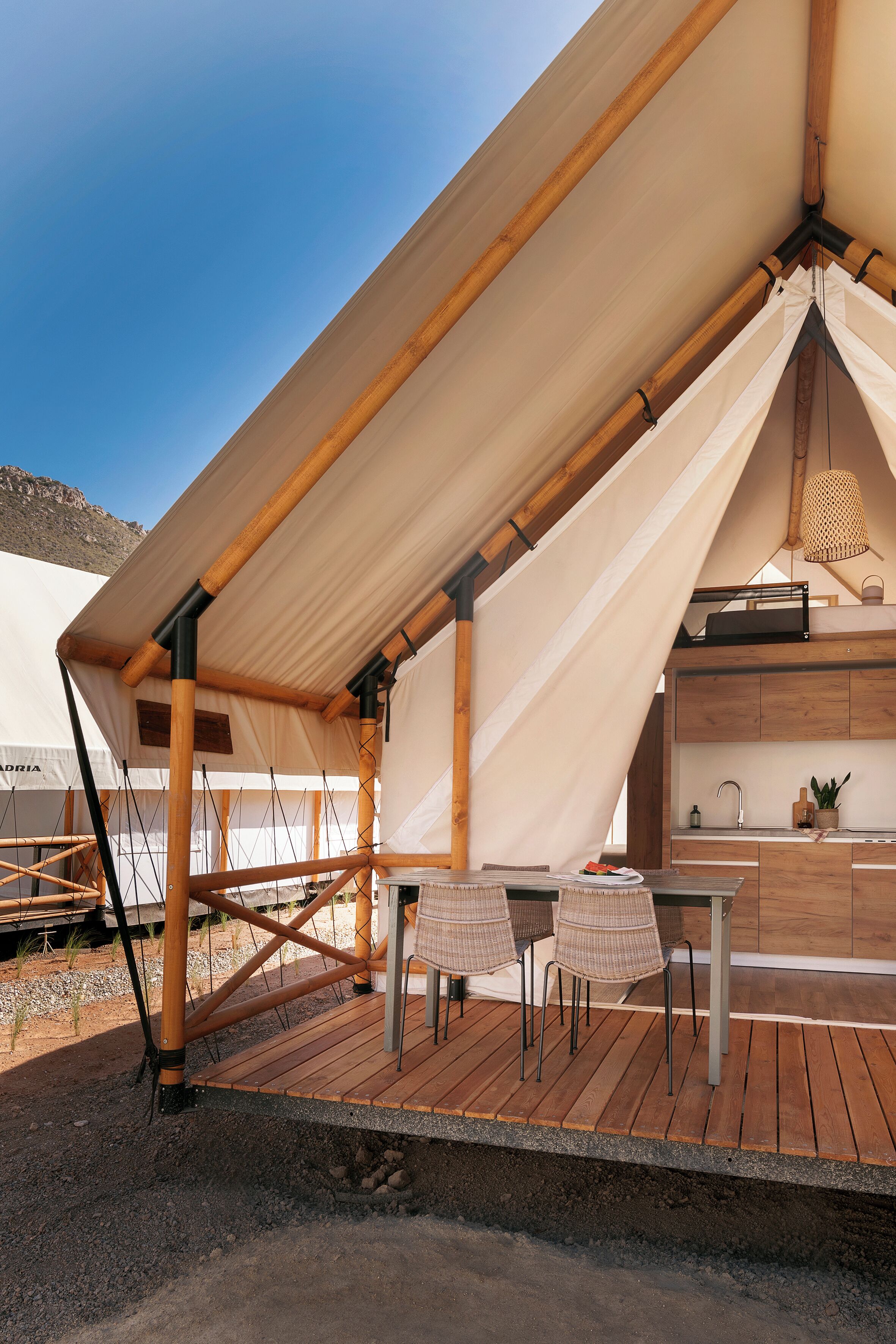 A tent with a wooden deck, a kitchen area, and a dining table with chairs.
