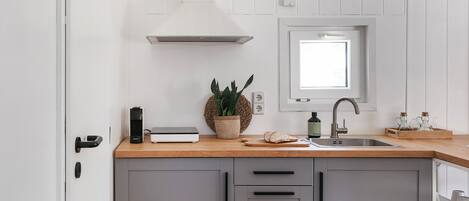 Una cocina moderna con encimera de madera, armarios grises, un ventanal sobre el fregadero y una puerta blanca.