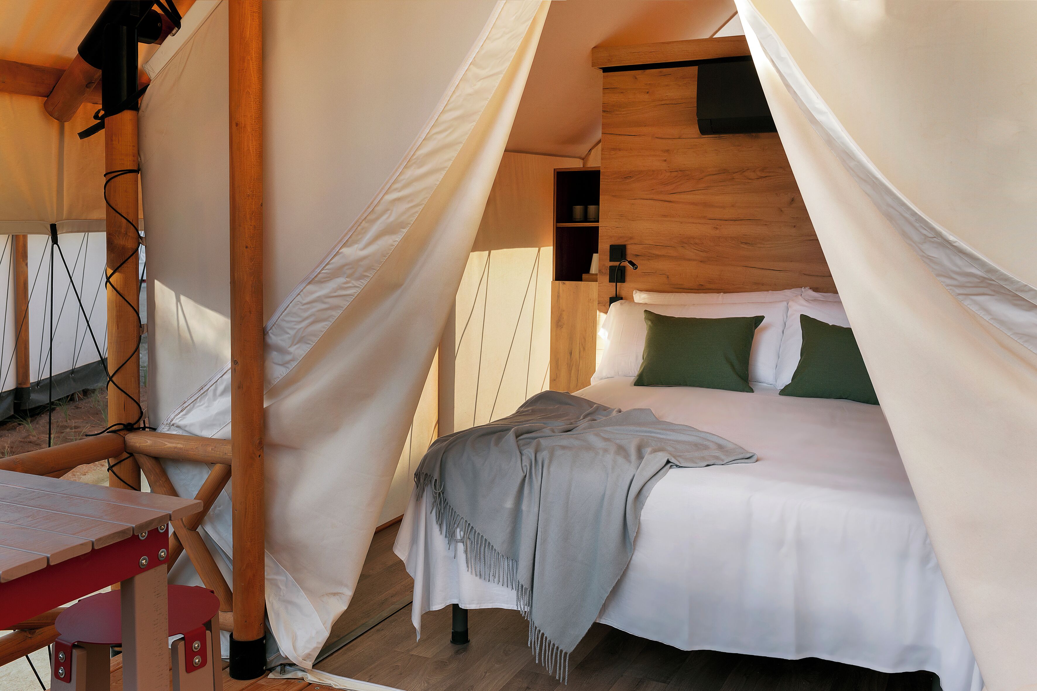 A tented accommodation with a bed, a table, and a shelf.