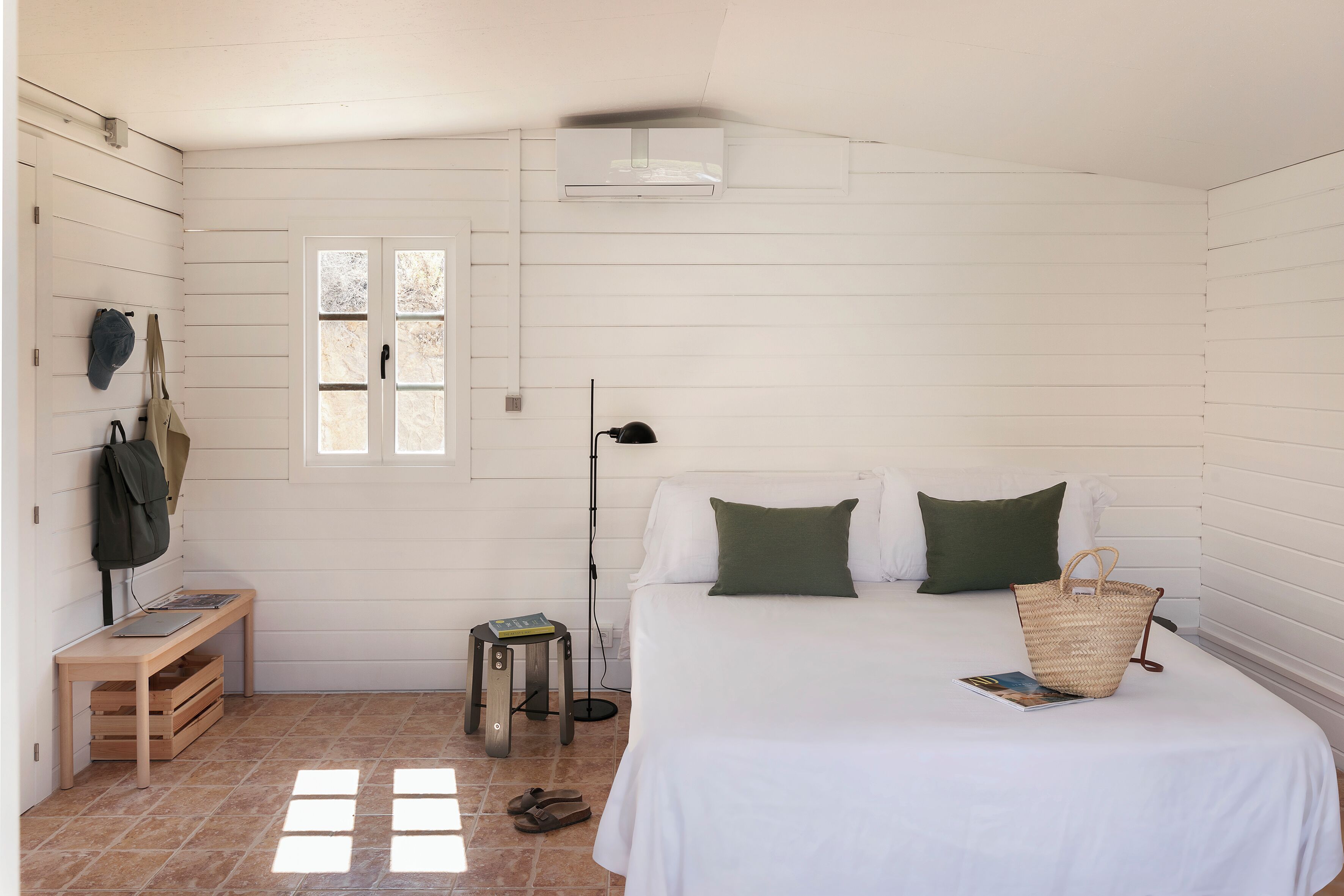 Et soveværelse med seng, puder, et sengebord, en lampe, et vindue og en vægmonteret aircondition.
