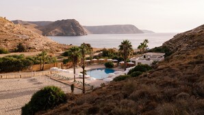 A pool area with lounge chairs and umbrellas, surrounded by hills and a view of the sea. - wecamp Cabo de Gata (Nijar)