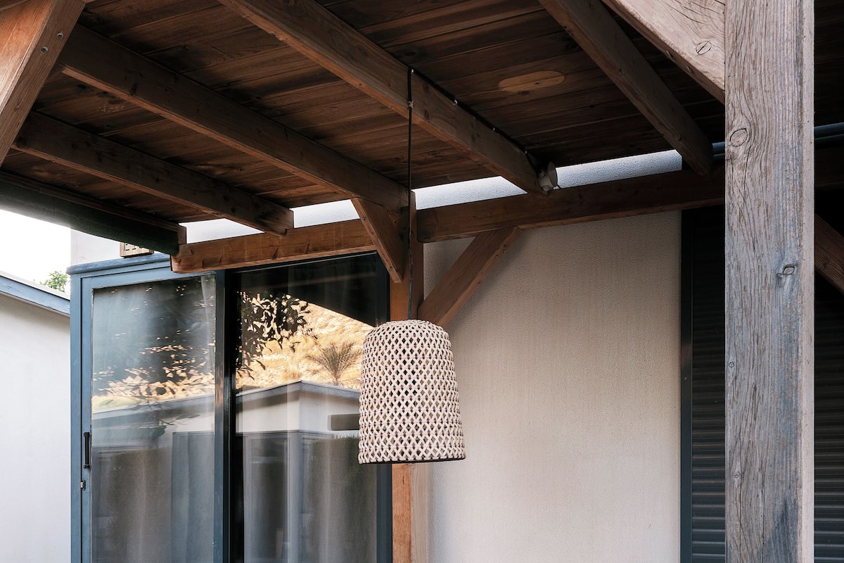 An outdoor patio with a wooden ceiling, a glass door, and a table with chairs.