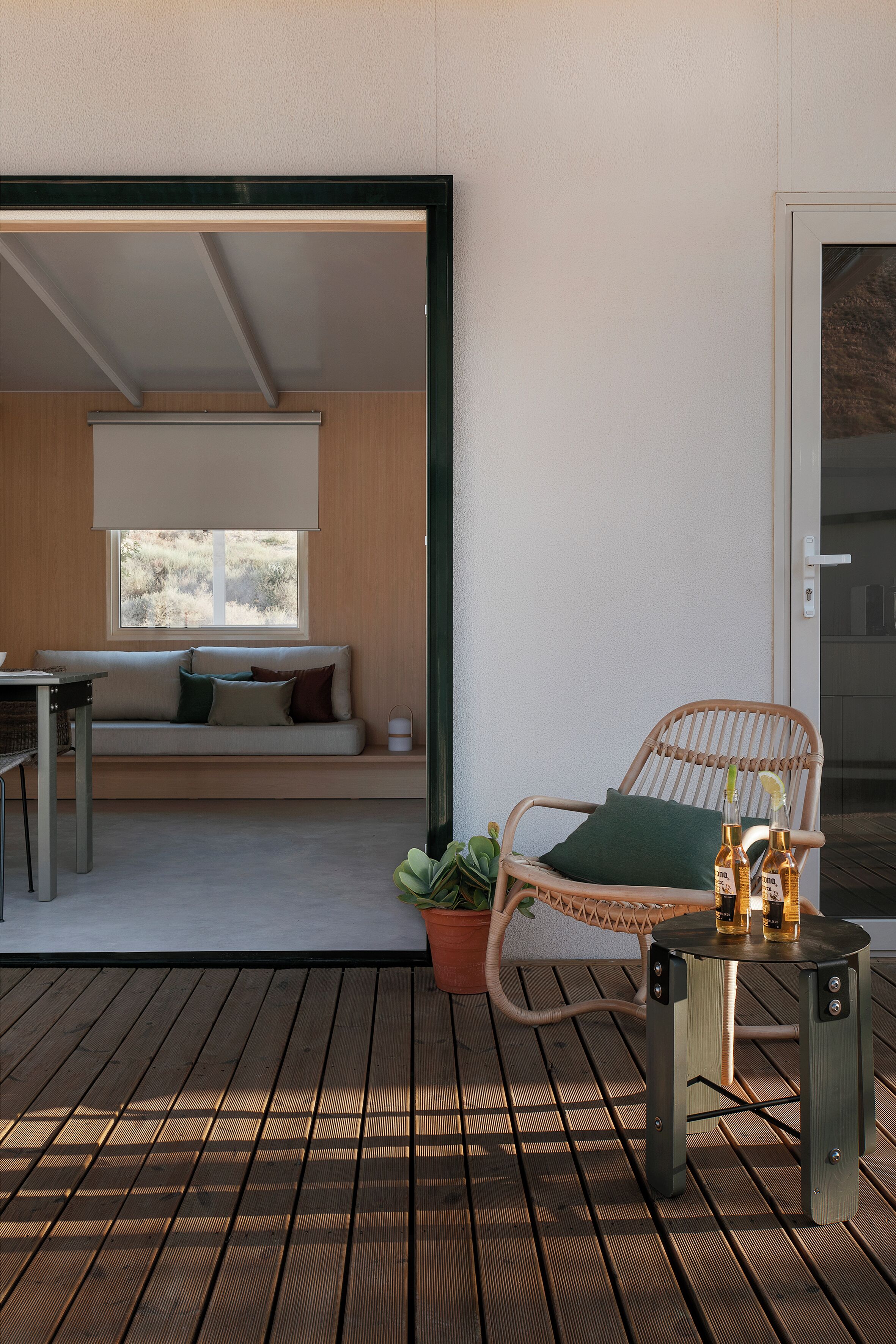 A wooden deck with a wicker chair and a small table, a sofa with cushions, and a potted plant.