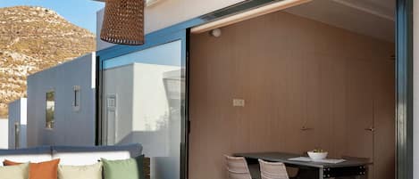 An outdoor seating area with a wooden deck, a wicker chair, a table with a bottle, and a glass partition wall.