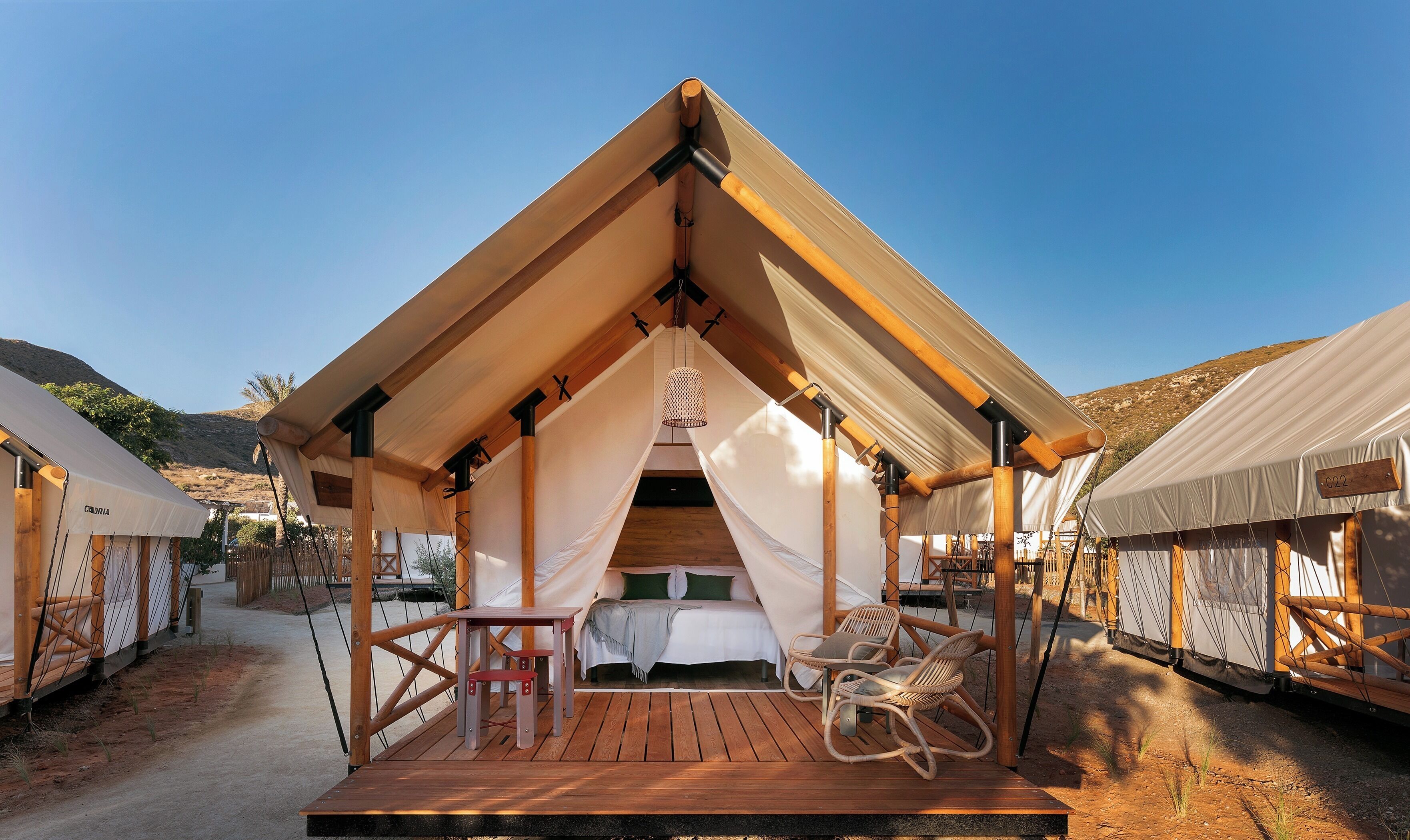 Alojamento em tenda com um deck de madeira, uma cama com almofadas e um candeeiro suspenso.