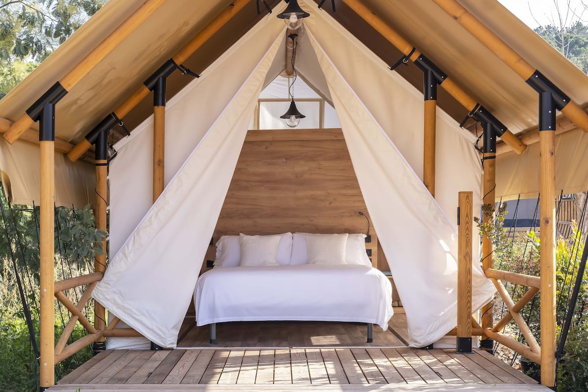 A tented accommodation with a bed, wooden beams, and a hanging light fixture.