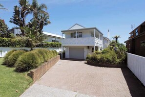 A two-story house with a balcony, surrounded by well-maintained gardens and a paved driveway. - Awesome Beach House, stroll to Town and Beach (Mount Maunganui)