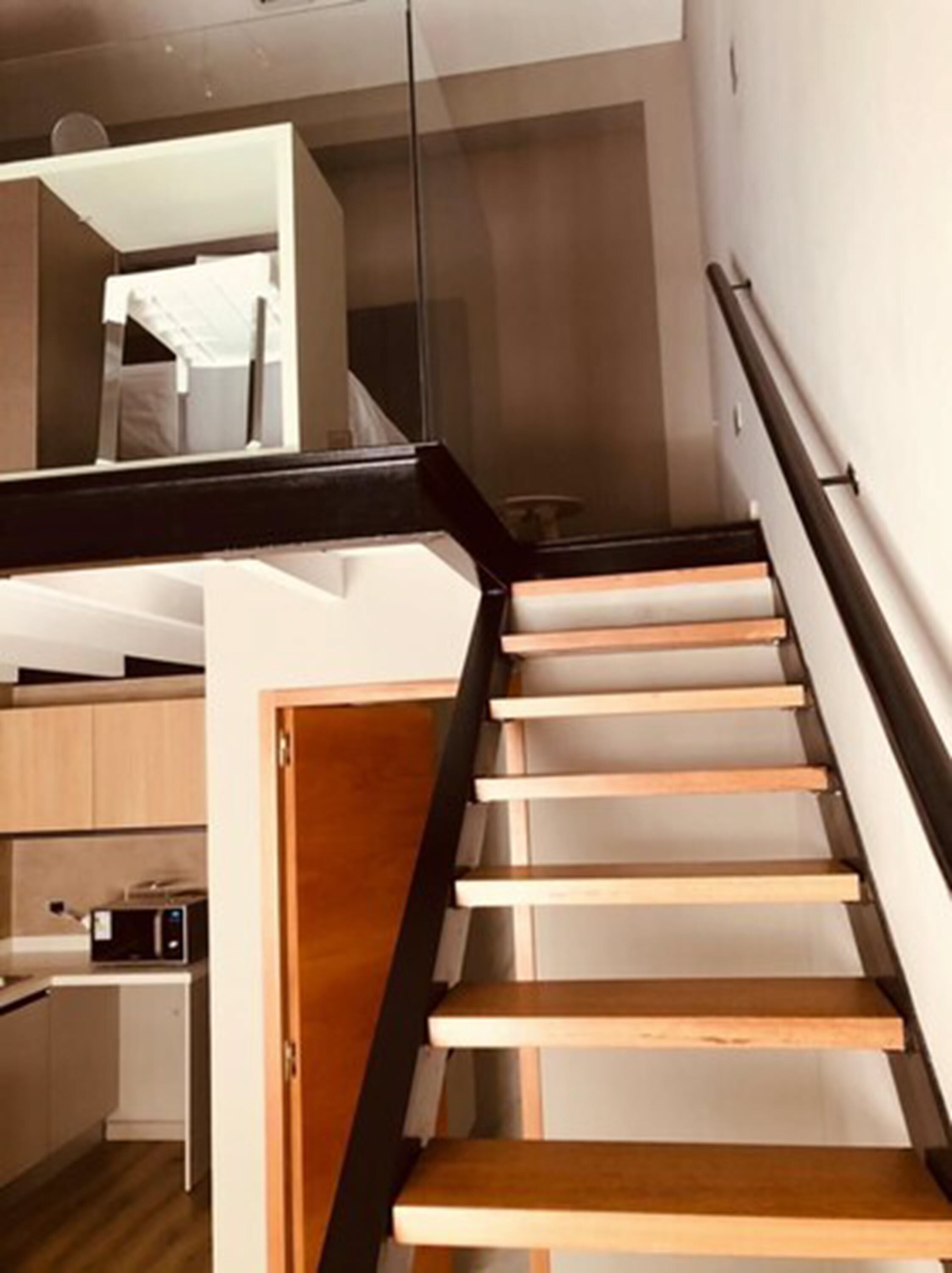 A modern staircase with wooden steps and a black handrail leading to an upper floor.