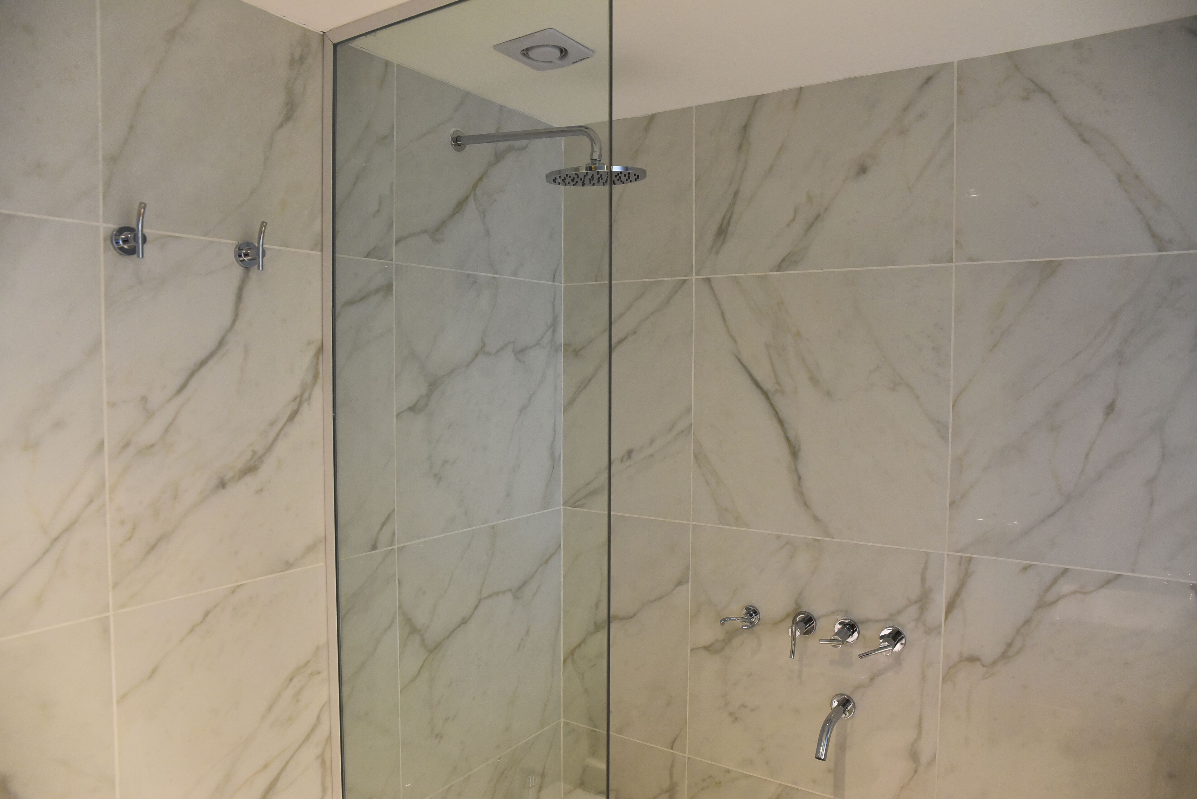 Un baño moderno con cabina de ducha de vidrio, baldosas de mármol y un cabezal de ducha manual.