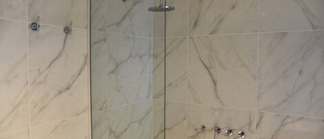 Un baño moderno con cabina de ducha de vidrio, baldosas de mármol y un cabezal de ducha manual.