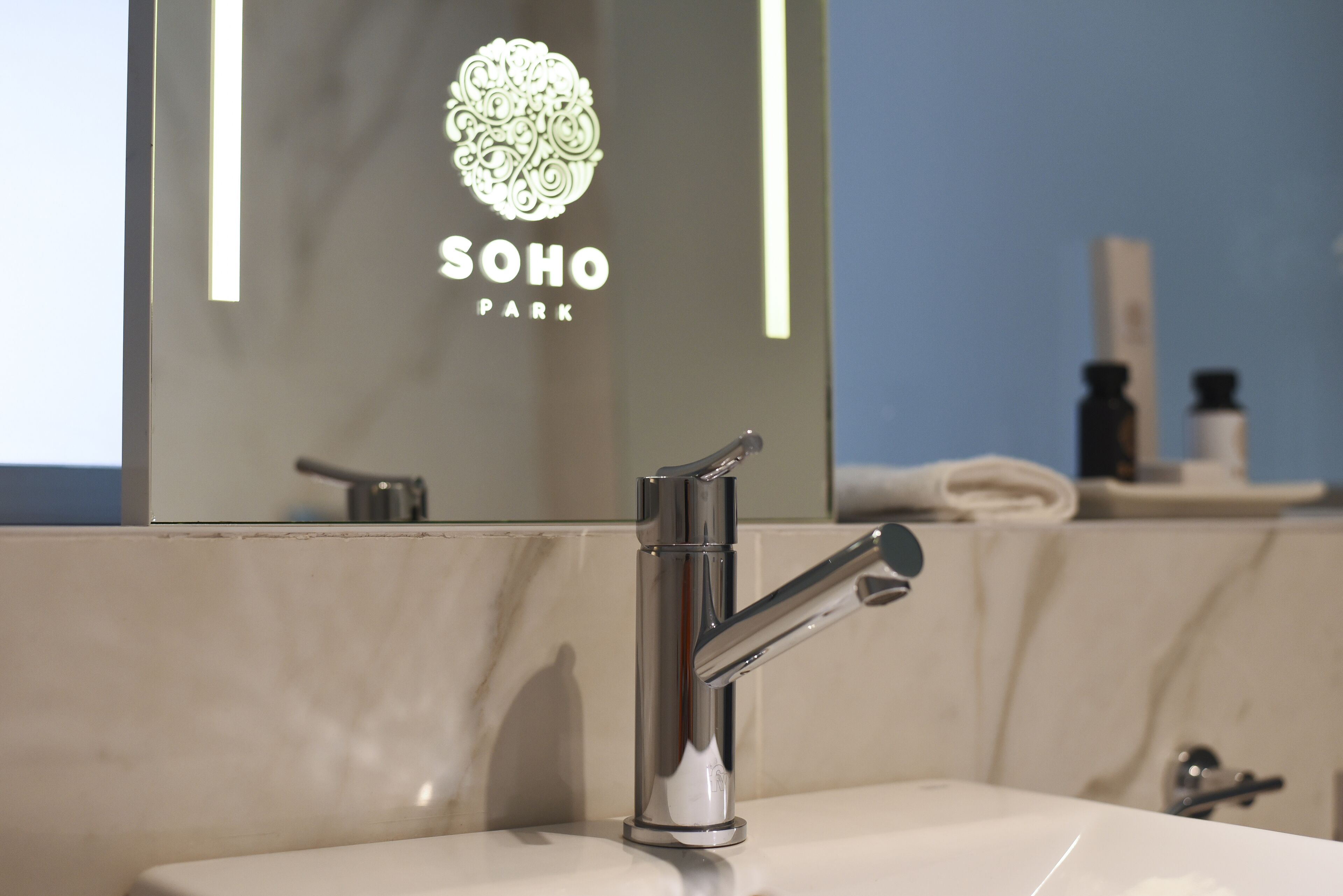 A modern bathroom with a chrome faucet, a mirror reflecting a logo and text, and a marble countertop.