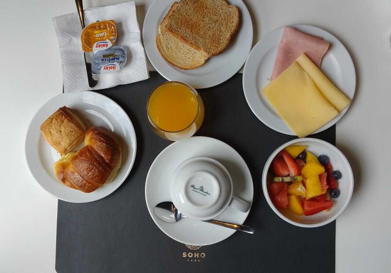 A breakfast setup with toast, ham, cheese, croissants, and a fruit bowl on a table.