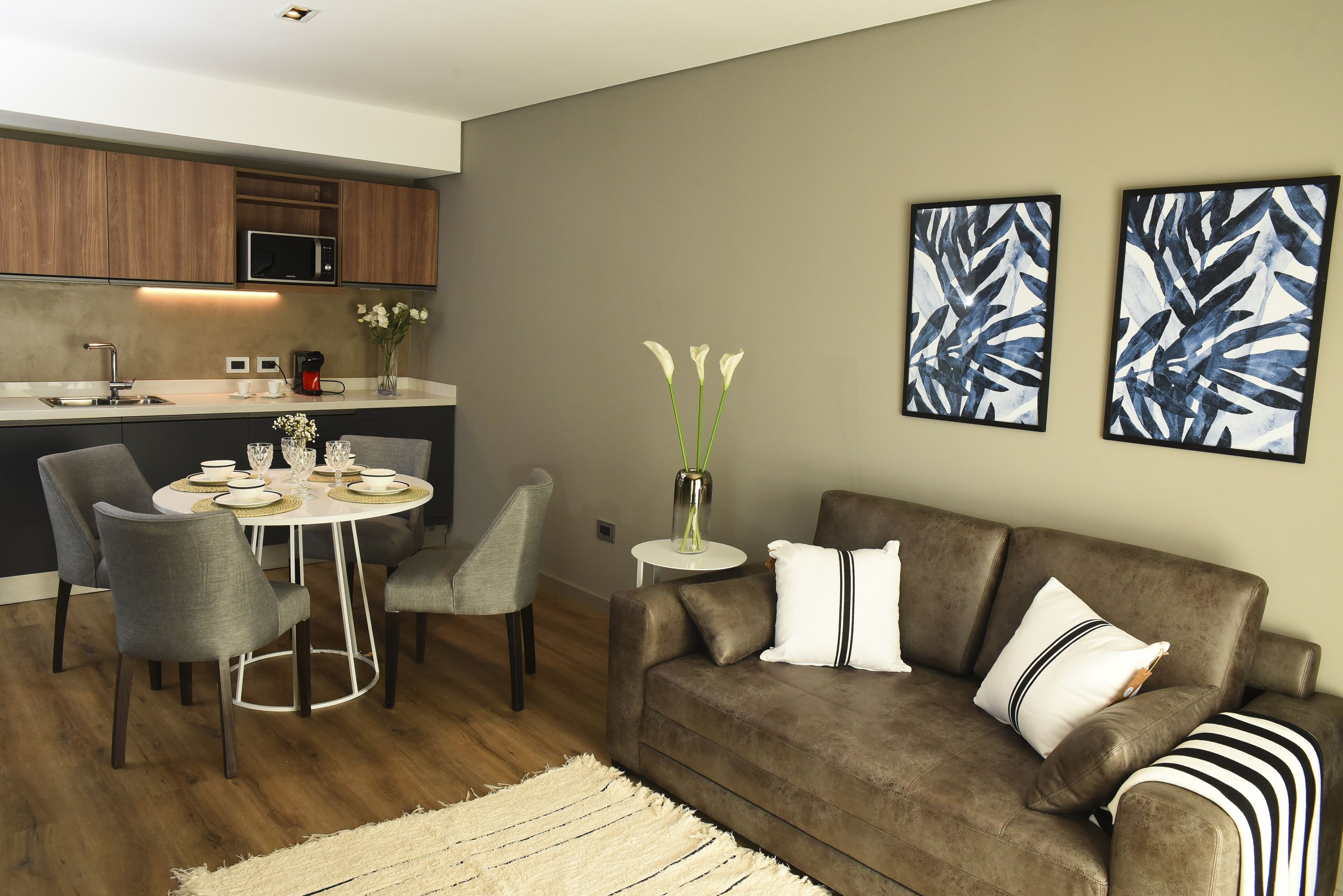 Un salon moderne avec un canapé marron, une table à manger avec des chaises, et un coin cuisine à l’arrière-plan.