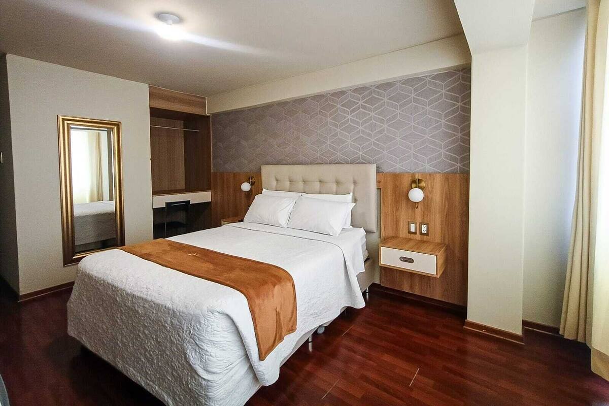 Une chambre d’hôtel avec un grand lit, une armoire, un miroir et une table de chevet.