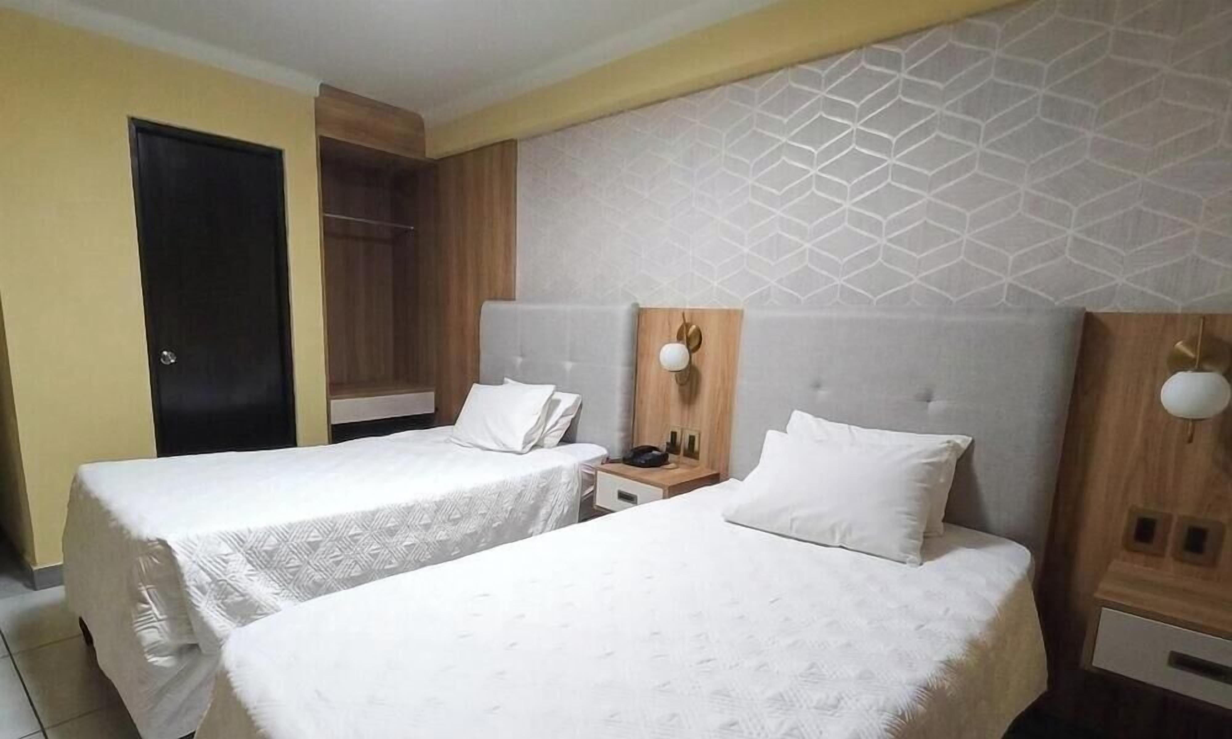 Una camera d'albergo con due letti, un armadio, un comodino con lampada e una parete decorata.