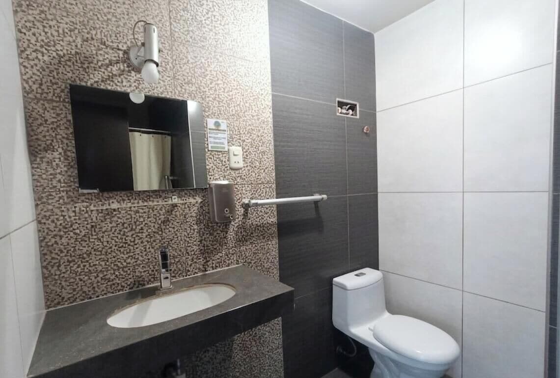 Een badkamer met een wastafel, spiegel, zeepdispenser en toilet.