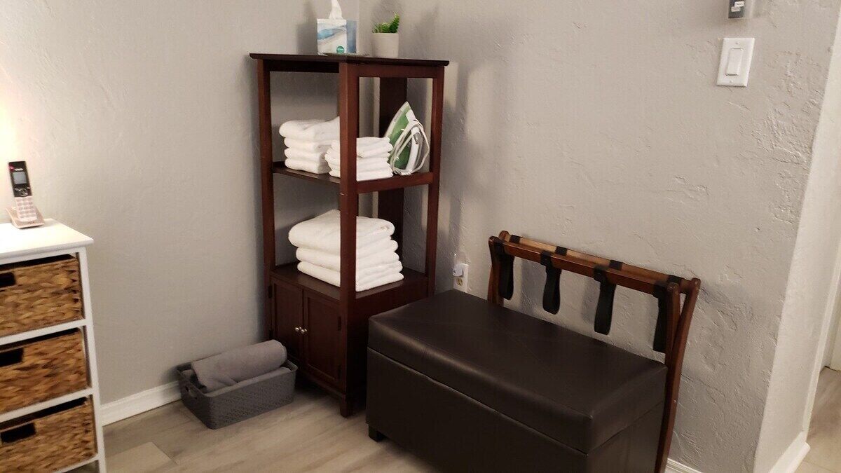 Un baño con un banco de madera, un estante con toallas y un pequeño cubo de basura.