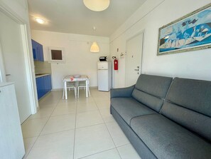 A compact living space with a kitchenette, a dining table, a gray sofa, and a painting on the wall. - Modern apartment in a quiet area (Porto Santa Margherita)