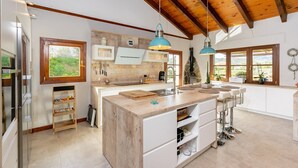 A spacious kitchen with a large island, wooden ceiling beams, and large windows offering views of the outdoors. - Design villa in Cala de Mijas (La Cala de Mijas)