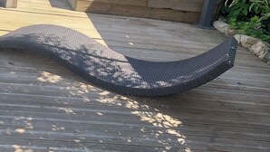 Une terrasse en bois dotée d’un espace salon extérieur incurvé et noir, d’une clôture en bambou et d’un petit jardin agrémenté de diverses plantes et d’une statue.