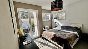 Une chambre à coucher avec un lit, un bureau, une chaise, une lampe et une vue sur l’extérieur.