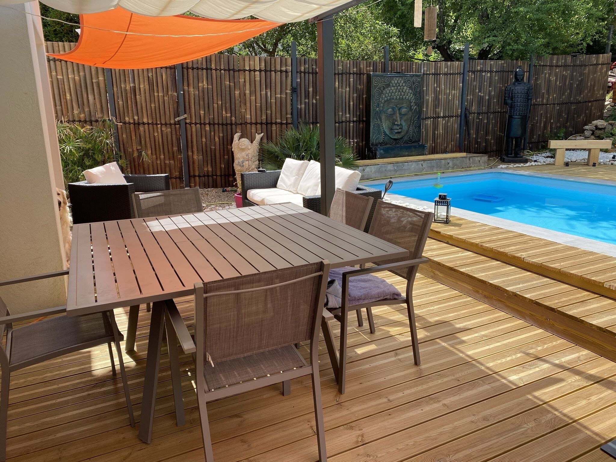 Une terrasse extérieure avec une table et des chaises en bois, une piscine et une clôture en bambou.