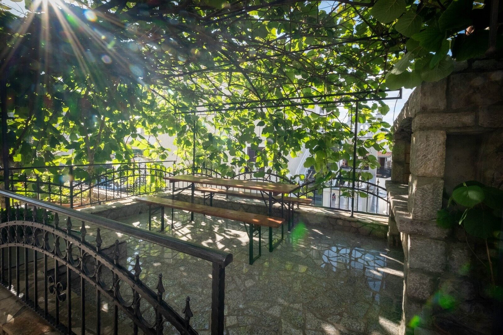 Un espace extérieur aménagé en terrasse, doté d’un sol en pierre et de rampes en métal, entouré d’une végétation luxuriante et d’un mur en pierre.