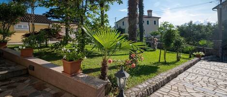 Ein Garten mit Blumentöpfen, einem Kiesweg und einem Gebäude im Hintergrund.