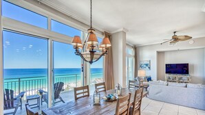 Ein geräumiger Wohnbereich mit großem Esstisch, bequemen Sitzgelegenheiten, einem Fernseher und einem Balkon mit Meerblick.