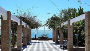 A covered walkway with brick pillars and a checkered floor, leading to a bench and a view of the sea. - South Apartment, in Torrecilla Nerja (Nerja)