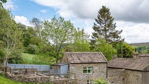 A stone cottage with a stone patio, a small shed, and a wooden deck with chairs.