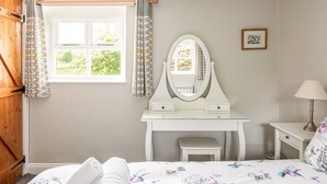 A bedroom with a bed, a white dresser with a mirror, a window with curtains, and a lamp.