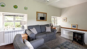 A living room with a grey sofa, a wooden coffee table, a black stove, and a large window with white blinds.