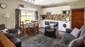 A compact living space with a dining area, a sofa, a chair, a washing machine, and a kitchen with cabinets and a microwave.