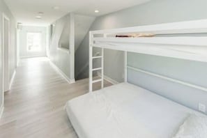 A room with bunk beds, a wooden ladder, and a hallway leading to another room.