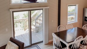 Ein Essbereich mit Holztisch und weißen Stühlen, ein Modell eines Segelbootes über einem Fenster und ein Deckenventilator.