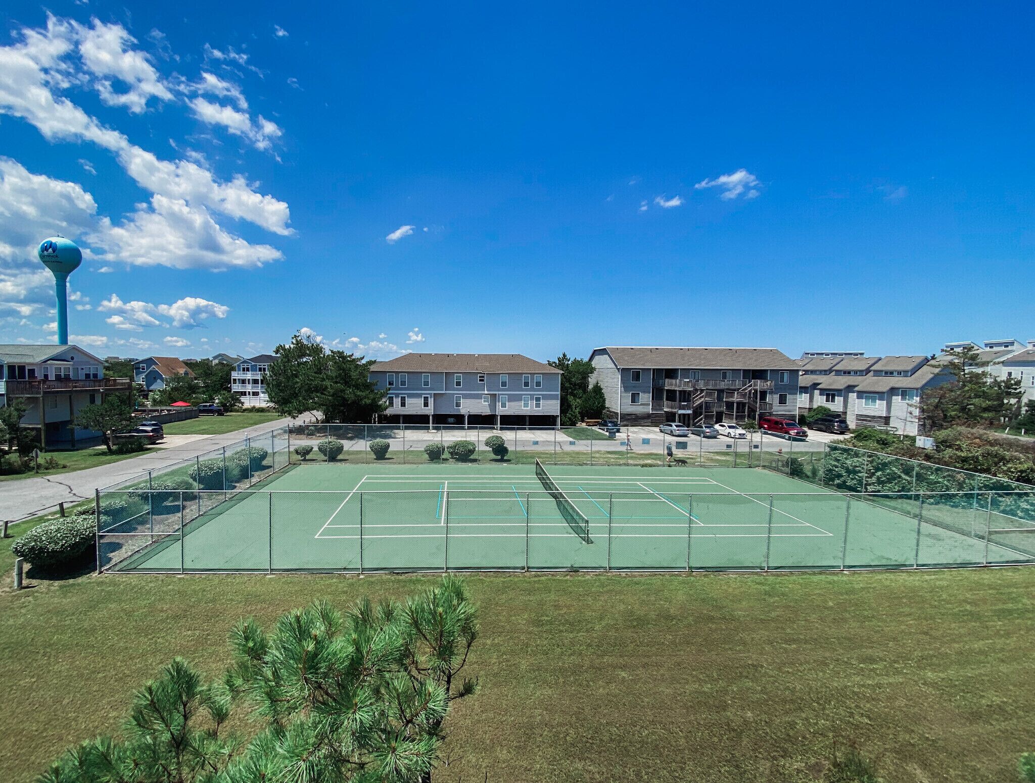 A tennis court surrounded by residential buildings, a water tower, and a clear blue sky.