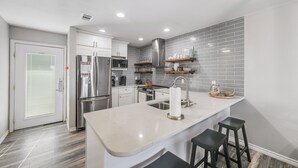 A modern kitchen with a central island, stainless steel appliances, and grey tiled backsplash.