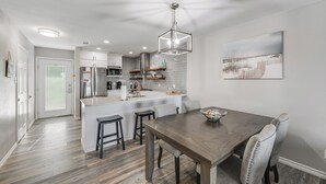 A modern kitchen with white cabinets, a central island, and a dining area with a wooden table and chairs.