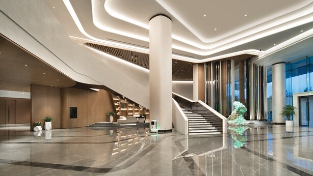 Un moderno vestíbulo con una escalera central, una mesa de recepción y una gran columna.