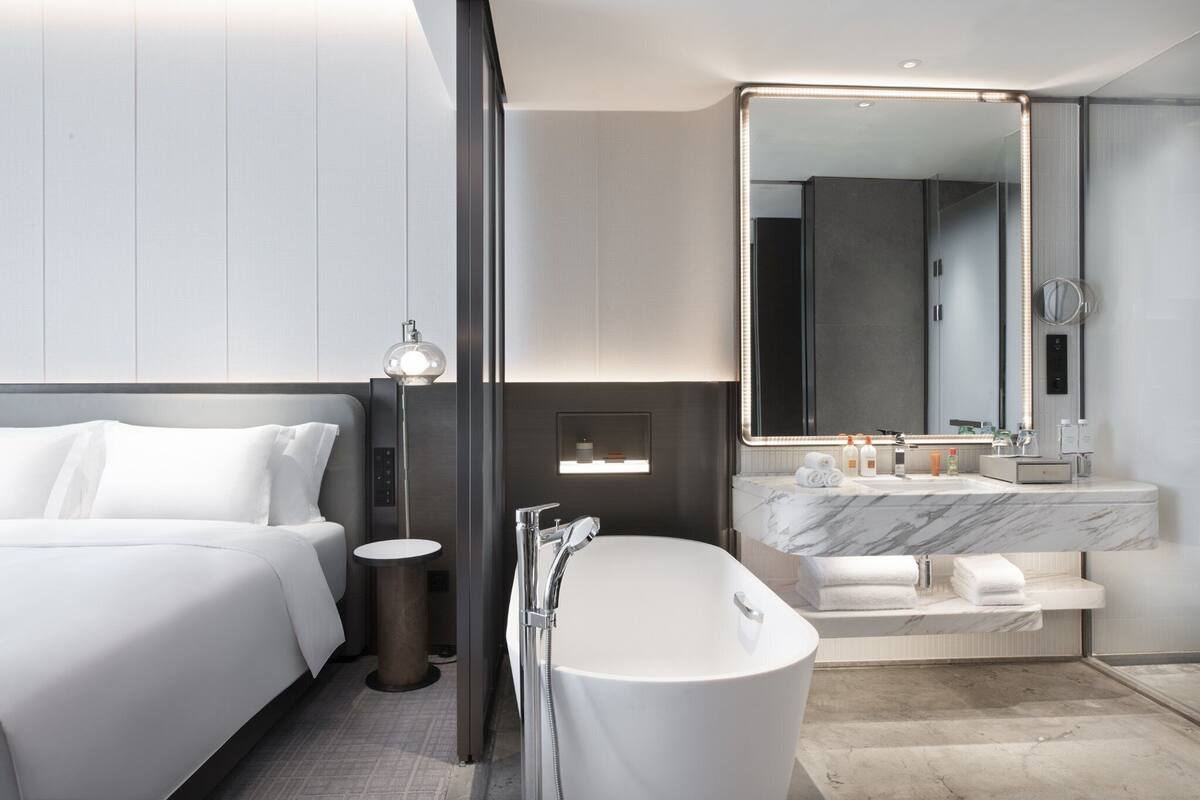 Ein modernes Hotelbad mit einer großzügigen Badewanne, einer separaten Duschkabine, einem Waschtisch mit Marmorplatte und einem großen Spiegel über dem Waschbecken.