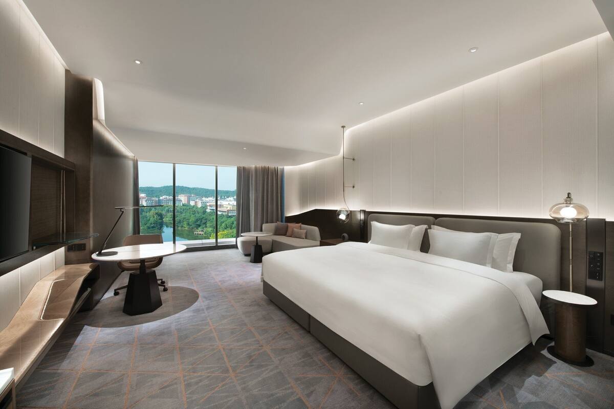Ein modernes Hotelzimmer mit einem großen Bett, einem Schreibtisch und Blick auf die Stadt.