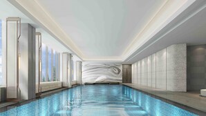 Una piscina interior moderna con superficie de agua azul cristalina, rodeada de techos altos y grandes ventanales.