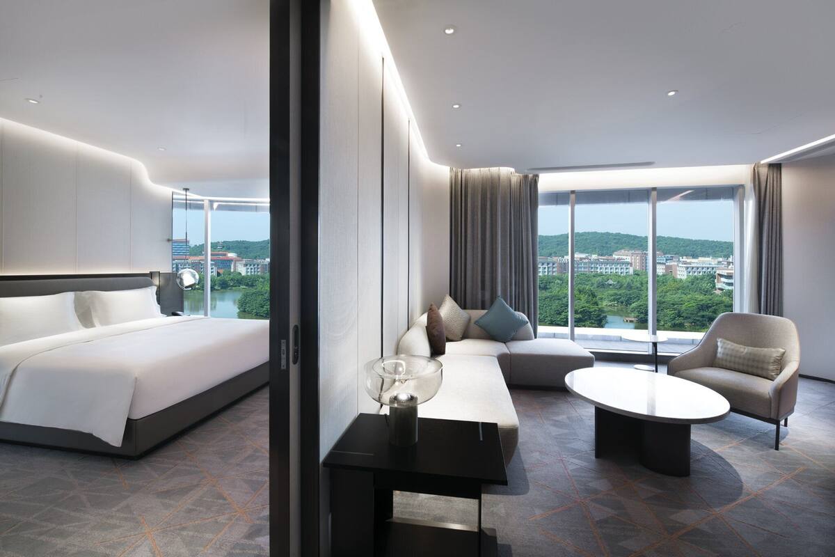 Ein modernes Hotelzimmer mit einem großen Bett, einem Sofa, einem Couchtisch und Blick auf die Stadt.