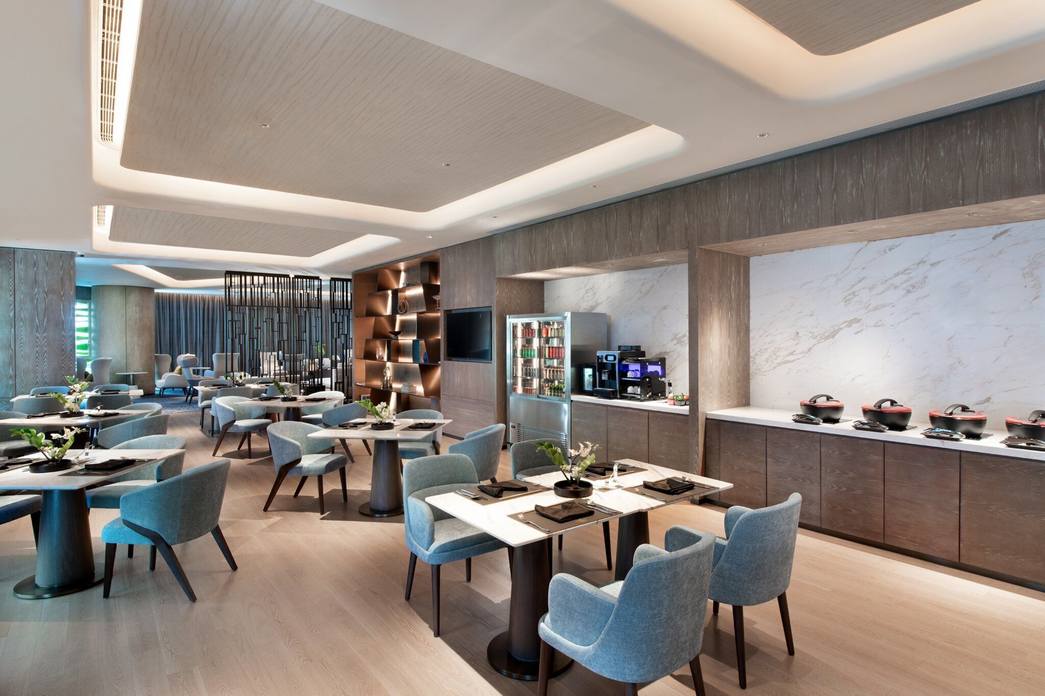 Um restaurante moderno com várias mesas e cadeiras, área de cozinha com painel de mármore e diversos eletrodomésticos.