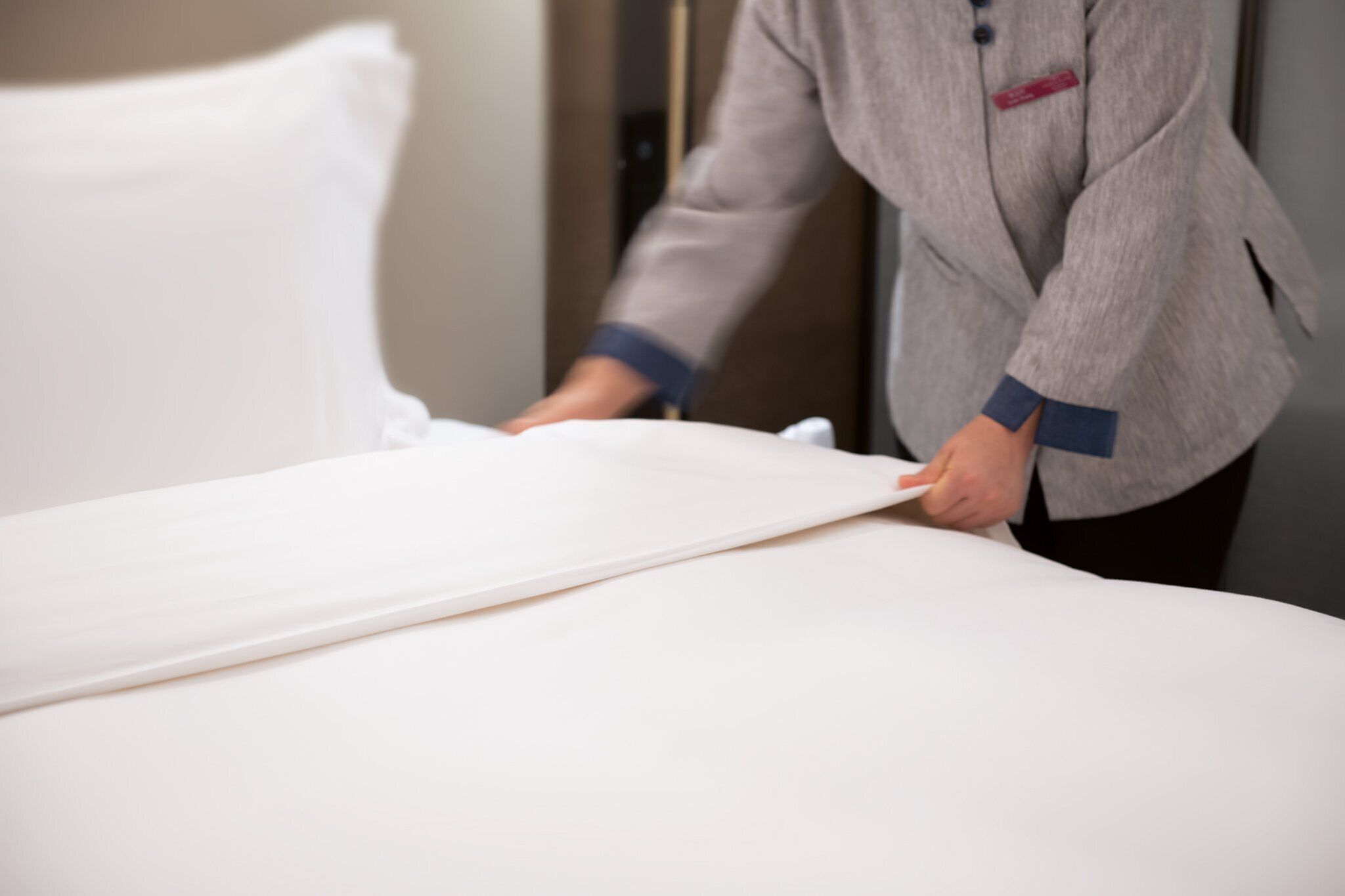 A person adjusting a bed in a hotel room.