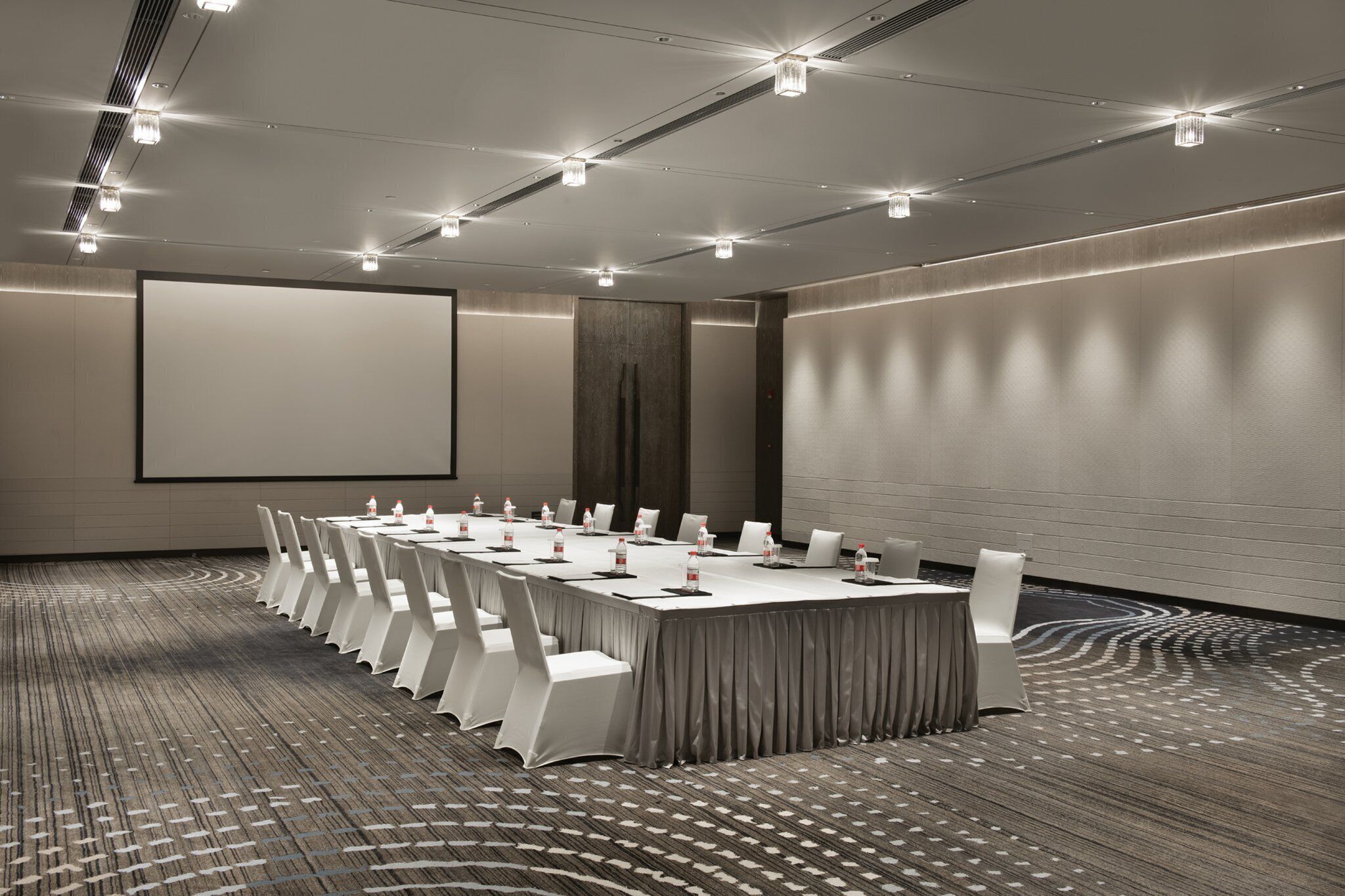 Ein Konferenzraum mit einem langen Tisch, Stühlen, einer Projektionsleinwand und einem Teppichboden.