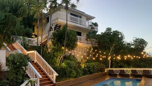 A pool area with a wooden deck, a pool, and a staircase leading to a balcony. - The Breeze USVI (St. Thomas)