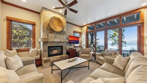 A spacious living room with a stone fireplace, comfortable seating, and large windows offering a view of the outdoors.